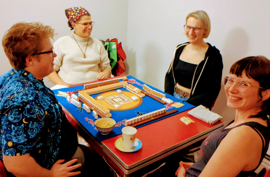 Four mahjong players seated around red table